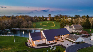 Luxury barn wedding venue in Lancaster Pennsylvania with outdoor wedding ceremony by the water with green garden like landscapes surrounded by trees. 