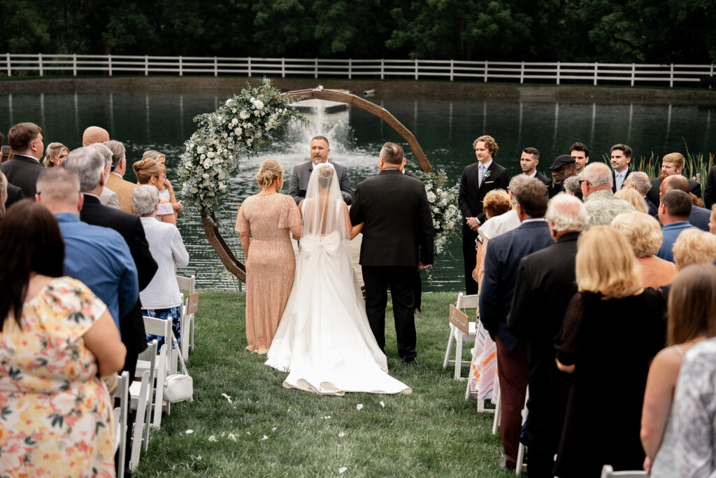 Bride walking down the aisle with her mother and father of the bride at our garden wedding ceremony with pond backdrop near Philly